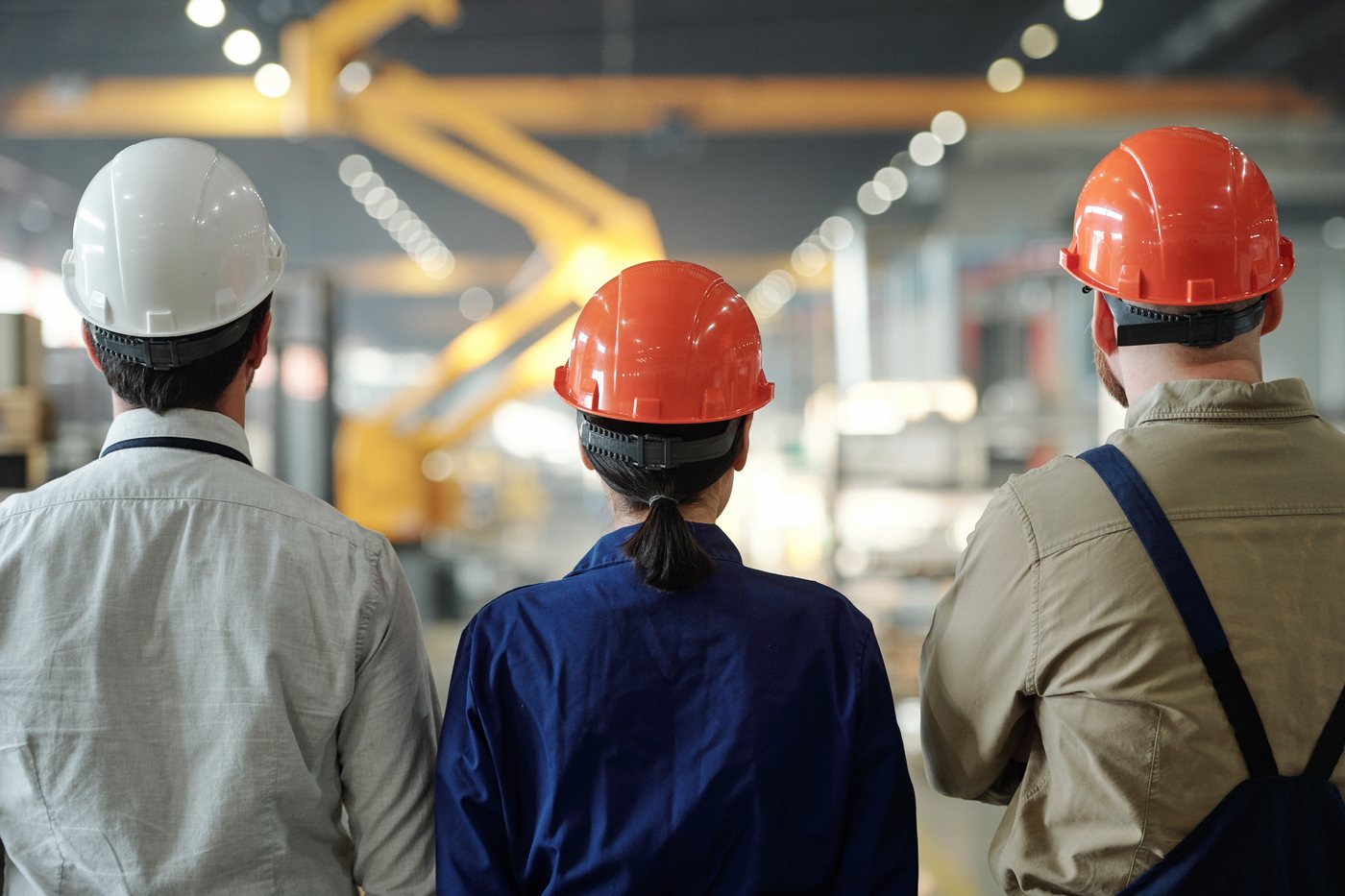 Three people in hard hats looking across a plant floor