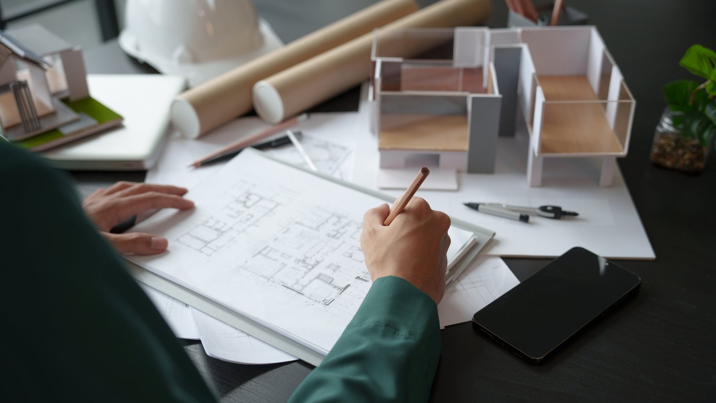 Hands drawing over floor plans beside an architectural model